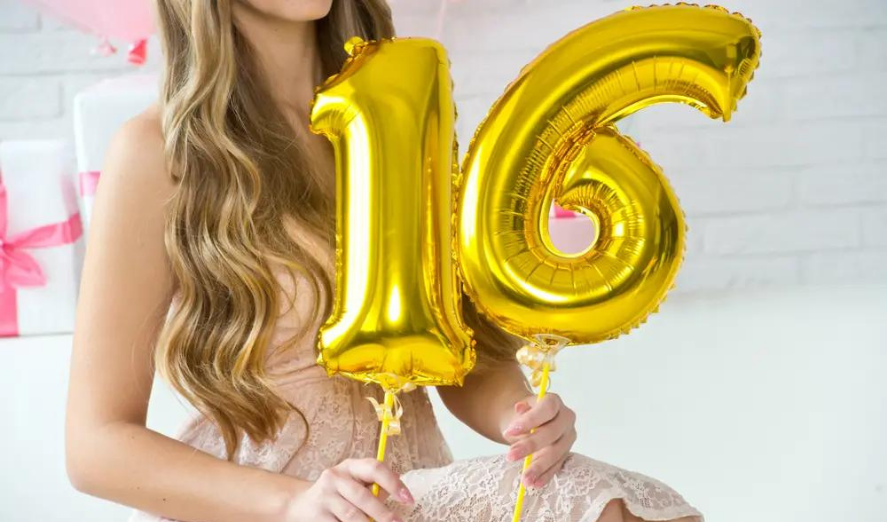 teenage girl holding up 16 gold number balloons to celebrate a sweet 16 party